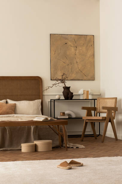 istock Creative composition of bedroom interior with mock up poster frame, cozy bed, beige bedding, rattan armchair, black rack, bright rug, vase with branch and personal accessories. Home decor. Template. 1716608940