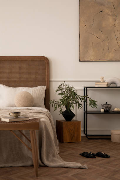 istock Warm bedroom interior with mock up poster frame, cozy bed, beige bedding round pillow, black rack, wall with stucco, wooden bench, slippers,  and personal accessories. Home decor. Template. 1716609472