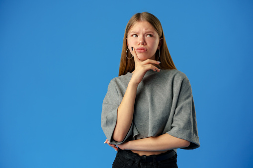 Young teen girl thinking about something over blue background in studio