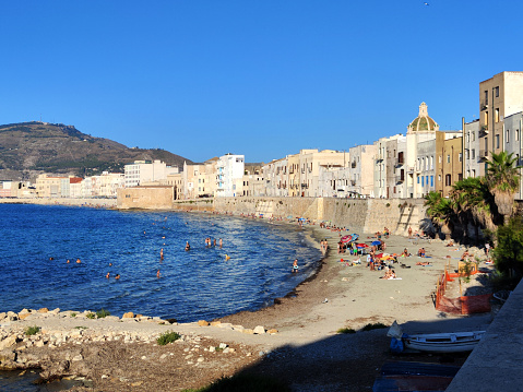People swimming at a public beach by the mura di Tramontana in the historic old town of Trapani, a city and municipality on the west coast of Sicily, in Italy.