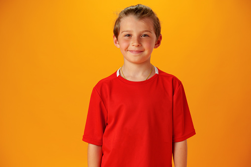 Smiling teen boy in red T-shirt against yellow background in studio