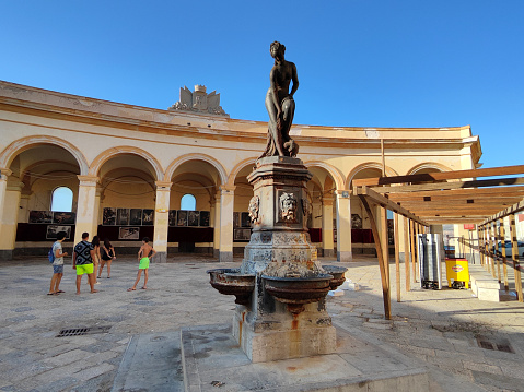 Group of local kids playing at the historical Piazza Mercato del Pesce, site of an old fish market and a historical fountain of venus in Trapani old town, Sicily.