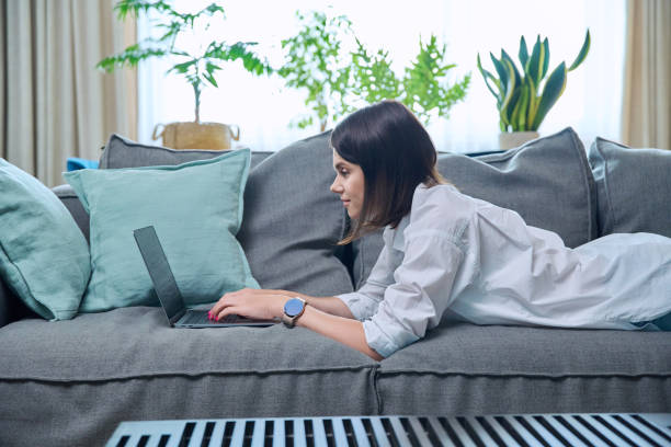 istock Young woman typing on laptop while lying on sofa at home 1716622833