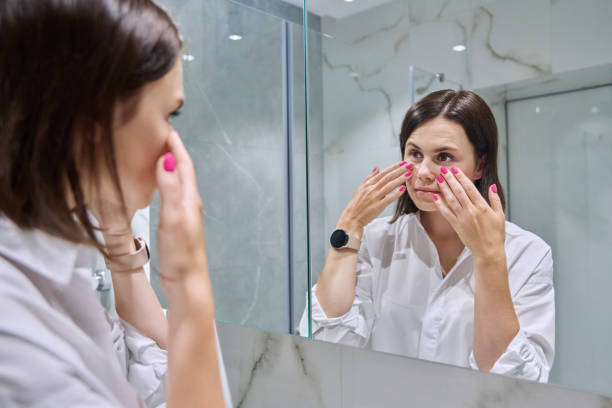 istock Young woman looking at her face in bathroom mirror 1716624988