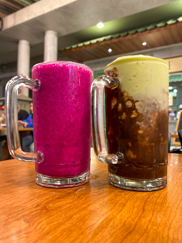 Two big glasses of red Dragon fruit  and green avocado juice drinks on wooden table in juice bar in Indonesia