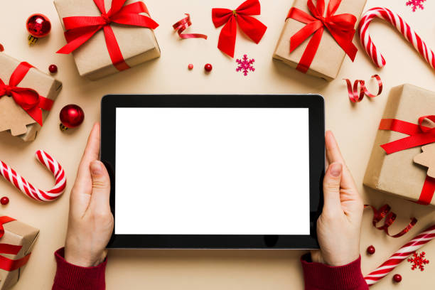 istock Christmas online shopping from home, female hands holding tablet pc with blank white display top view. woman hand holding tablet with blank screen, Christmas tree and gifts on background 1716637097