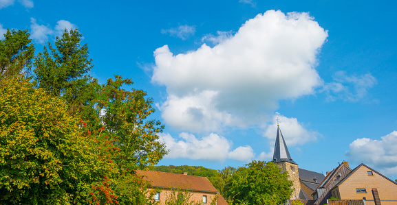 Tower of an ancient church in bright sunlight in a blue cloudy sky in autumn, Voeren, Limburg, Belgium, September 2023