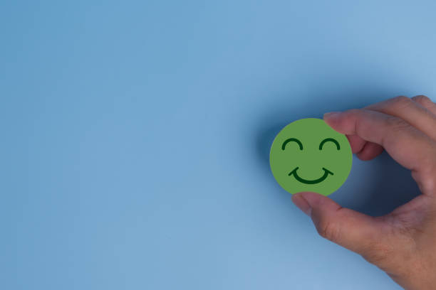 istock customer service evaluation and satisfaction survey concept. hand holding emotion happy smile face icon on wooden cube on blue background. copy space 1716651530