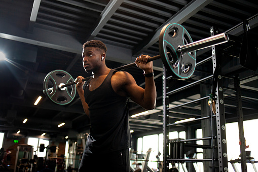 young african american man lifts barbell in dark gym, sports guy trains in fitness room and goes in for sports