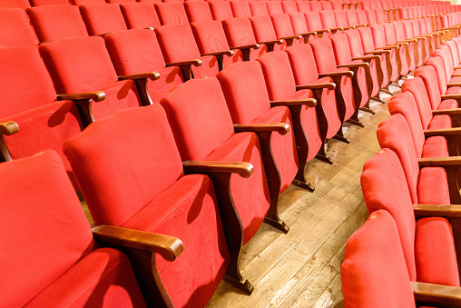 Row of red seats in a theater with old wooden floor.
