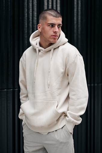 A young Caucasian male model wearing a white hoodie and posing on the street