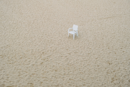 Beach in winter deserted with an abandoned plastic white chair, rubbish in nature.