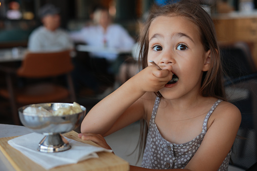 Little adorable preschool girl eating ice cream sundae in cup on sunny summer day. Happy toddler child eat icecream dessert. Sweet food on hot warm summertime days