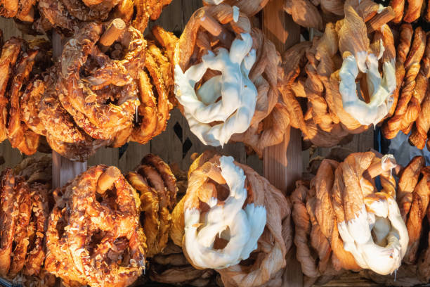 A bakery display case filled with hanging pretzels with various toppings. Chocolate, cheese, nuts. Background.