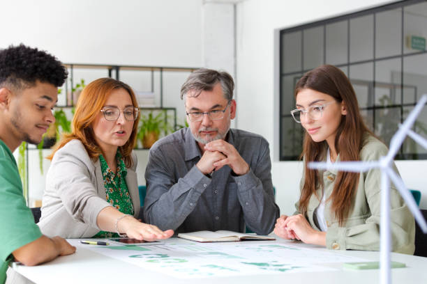 Business colleagues discussing over graph while sitting at desk with wind turbine models in office