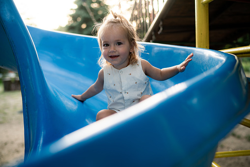 A happy toddler-age girl riding down the slide during summer day