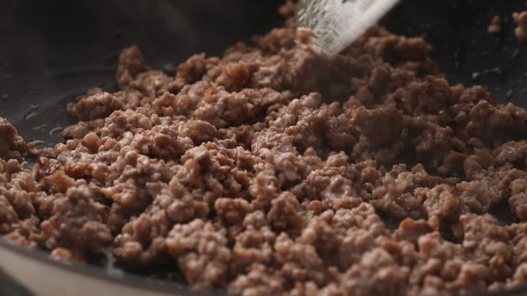 Man frying minced meat in a frying pan stirring with a spatula.