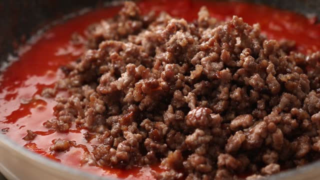 Adding fried minced meat to tomato sauce in a pan.