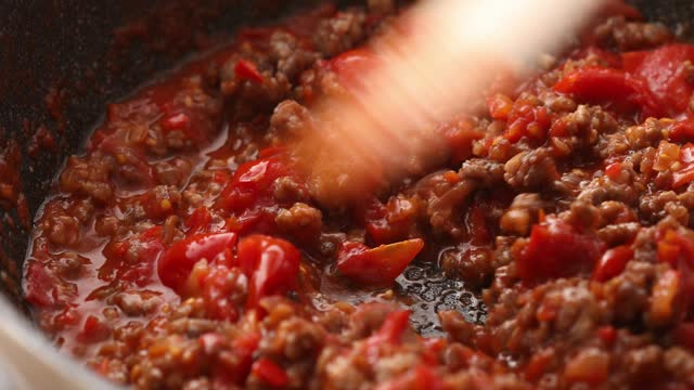 Stirring the fried minced meat and tomato sauce in a frying pan.