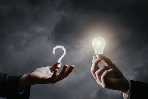 The concept of ideas for emerging questions. The hand gives an idea in the form of a burning light bulb to answer the question that has arisen.