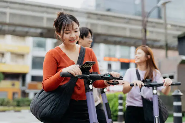 Young asian woman navigating with smartphone while riding an e-scooter