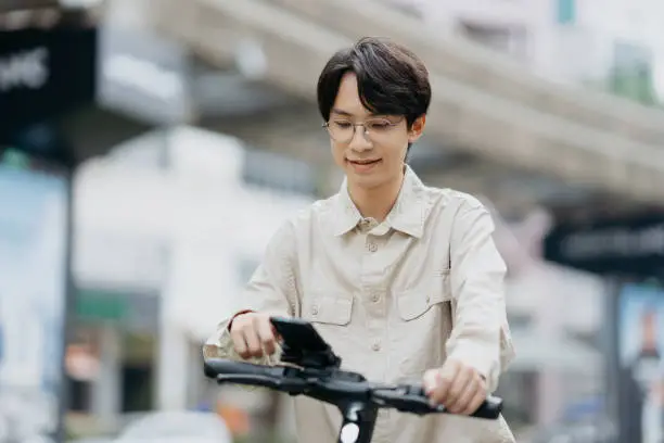 Young asian man navigating with smartphone while riding an e-scooter