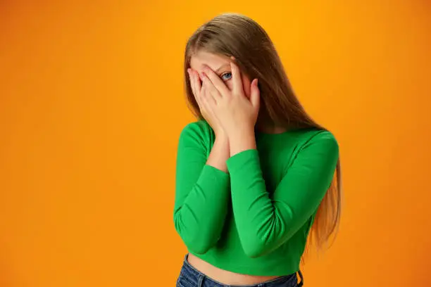 Teen girl over yellow background in studio shocked covering face with hands