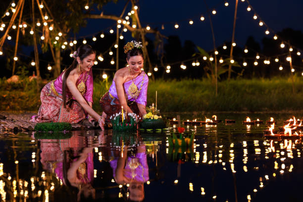 Two thai woman holding a krathong sitting on a raft by the river, Asian women in traditional Thai costumes bring krathongs to float on Loi Krathong Day, traditions and culture of Thailand, Loi Krathong Festival, Two thai woman holding a krathong sitting on a raft by the river, Asian women in traditional Thai costumes bring krathongs to float on Loi Krathong Day, traditions and culture of Thailand, loi krathong stock pictures, royalty-free photos & images