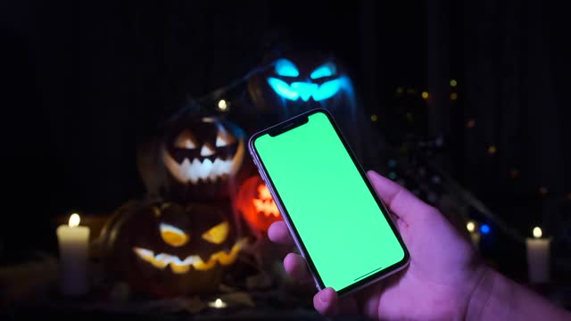 A hand holding a phone with a green screen at a party during Halloween