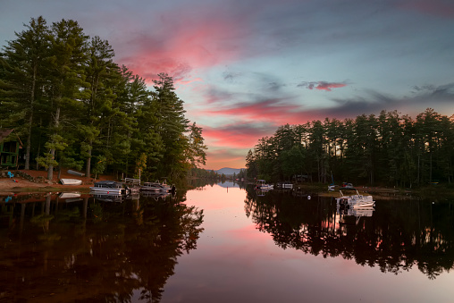 Calm lake with views of mountains and forest and small boats at sunset. Traditional look. USA. Maine.