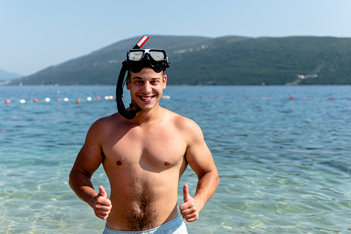 Amidst the gentle waves, a young man with diving glasses confidently showcases his passion for the mysteries beneath the sea's surface