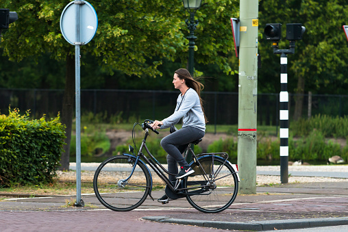 The Hague, Netherlands - July 8, 2015: A young woman with long hair, driving a black bicycle by one of the streets of the city.