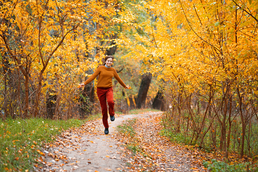 a young teenage girl walks in the autumn forest, goes along the road and enjoys the beautiful nature and bright yellow leaves
