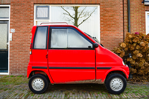 In Muiden, Netherlands a red Canta vehicle with two seats deigned for people with accessibility needs is small enough to park alongside the narrow brick streets.