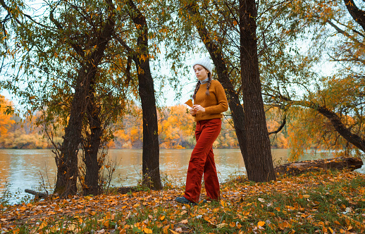 a young teenage girl walks through the autumn forest, walks along the riverbank and enjoys the beautiful nature and bright yellow leaves