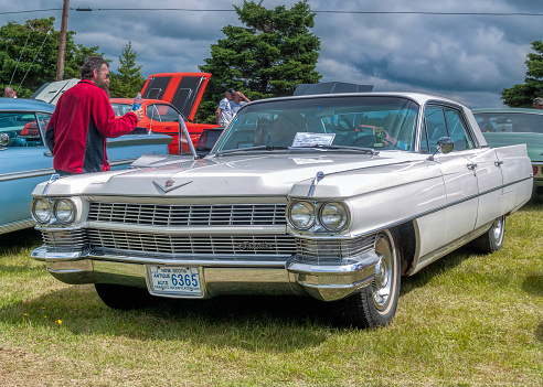 Chester, Nova Scotia, Canada - June 23, 2007 : 1964 Cadillac Coupe Deville. A man walks past the Cadillac holding a water bottle and gives the car a looking over. Graves Island Car Show at Graves Island Provincial Park, Chester, Nova Scotia Canada.