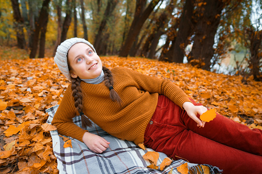 a young teenage girl is lying in a glade in the autumn forest, enjoying the beautiful nature and bright yellow leaves