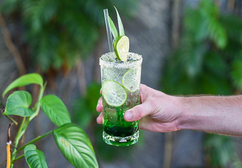 Hand holding panda leaves lemonade with desiccated coconut and green syrup on natural leaves background with copy space