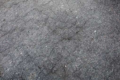 Broken grey asphalt road which is cracked. There are gravels on the black lines on the street. Close up transportation and construction background
