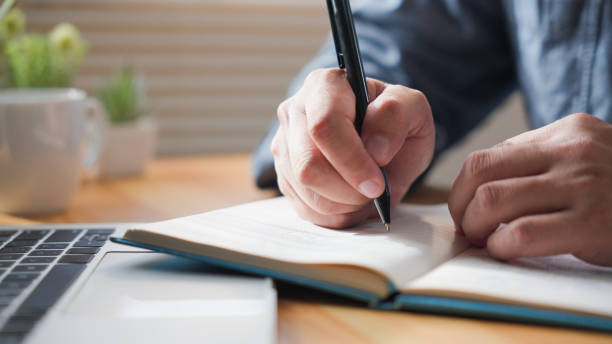 istock Unrecognized A man hand writing pen memo on notebook paper or letter, diary on table desk office. 1716978538