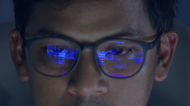 Close up head shot programmer person wearing eye glasses serious working and coding at night in office.