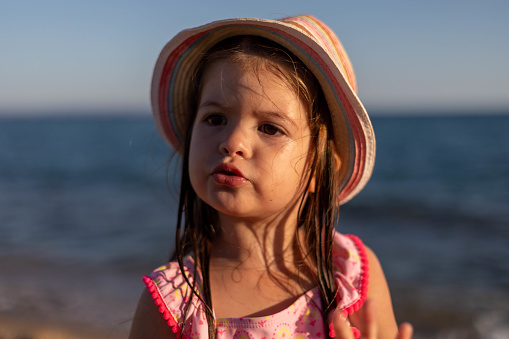 The little girl is standing on the seashore and trying to be serious. The portrait of a cute, three-year-old girl.