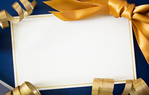 A blank card with gold and cream ribbons on a blue background, with copy space.