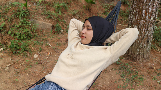 young muslim woman with headscarf sleeping in hammock on deck terrace during sunny summer afternoon.