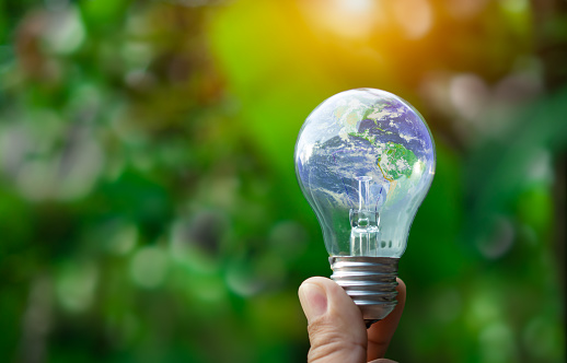 Concept of renewable energy, environmental protection, and sustainable renewable energy sources. World map on a light bulb set on a background nature green. Green energy.