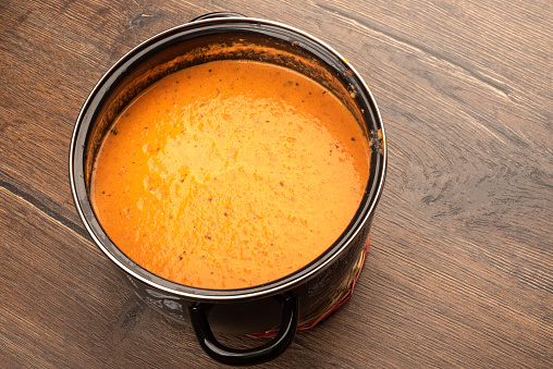 Pan full of tomato puree soup on a wooden background. Copy space.