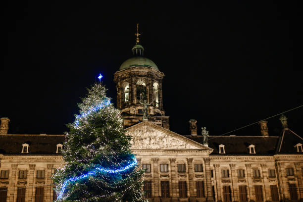 In Amsterdam, Netherlands a large Christmas tree is illuminated with lights in Dam Square in front of the Royal Palace.