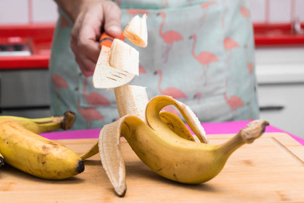 photo composition of woman in the kitchen cutting bananas into slices in the air with a knife. woman with the knife in her hand cutting a banana in the air. feminism concept - equal opportunity flash imagens e fotografias de stock