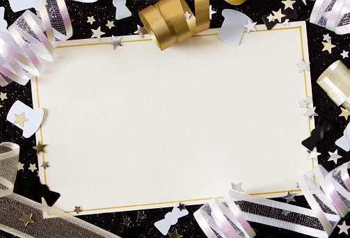 A blank card with gold and cream ribbons and stars on a black glitter background, with copy space.