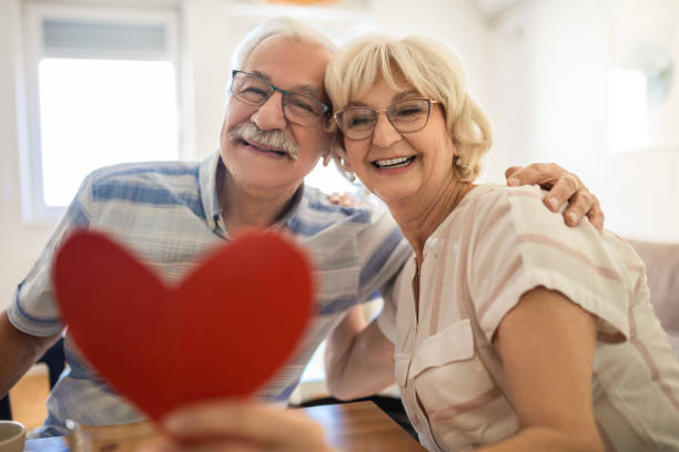 Celebrating Love Smiling senior woman receives present box and kissing her husband at home senior birthday card stock pictures, royalty-free photos & images